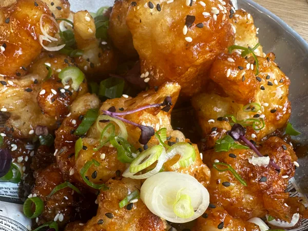 Sticky bloemkool met sesam, lente-ui en sweet chili in een schaal