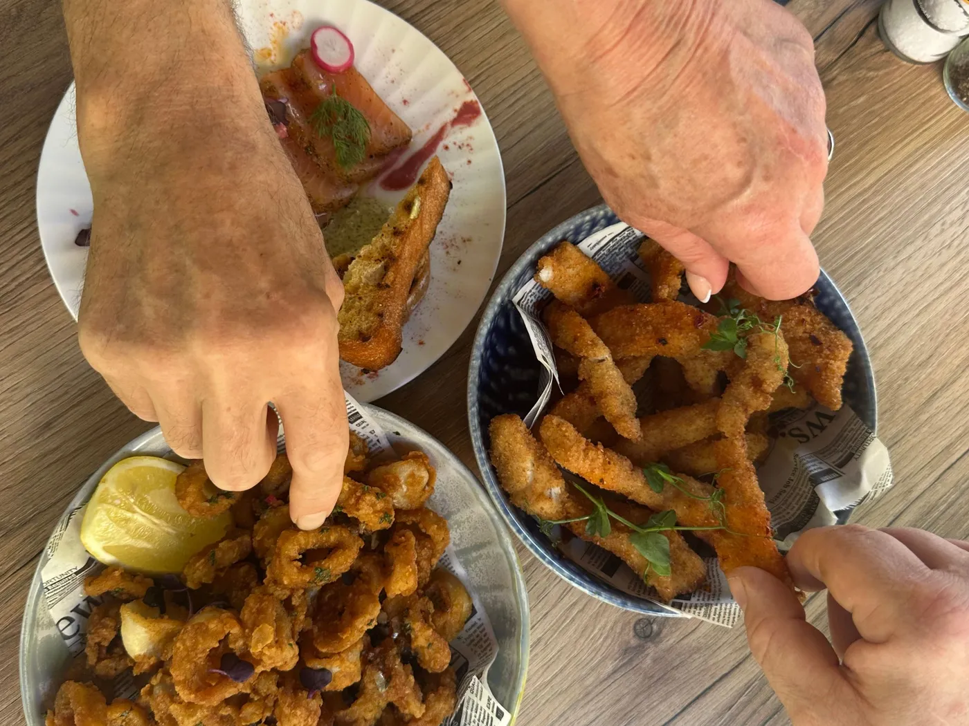 Drie handen die tegelijk uit twee schalen gefrituurde zeevruchten nemen