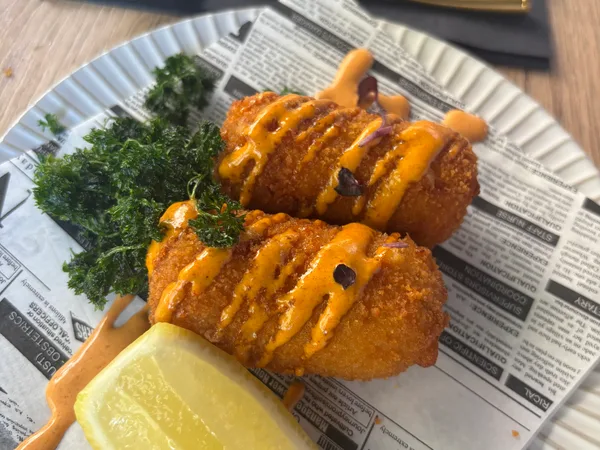 Twee kroketten op krantenpapier met een partje citroen en pittige saus