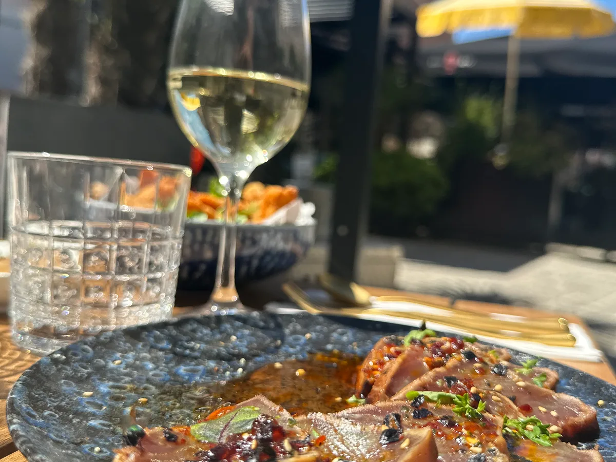 Bord met dun gesneden vis en een glas witte wijn op het terras