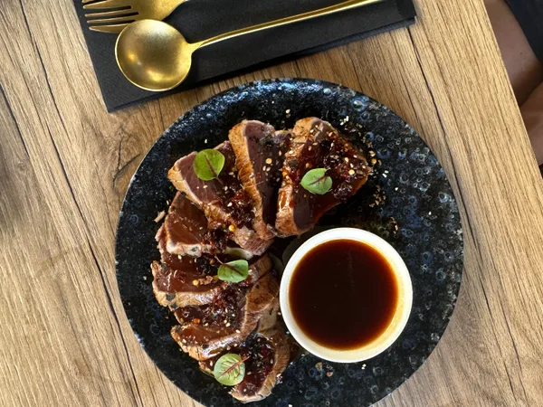 Dun gesneden vlees met sesam rond een kommetje donkere saus