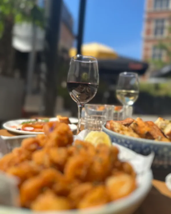 Schaal gefrituurde vis op het terras, met een glas witte wijn erachter
